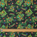 Close-up detail of TMNT scrub cap fabric showing green turtles, pizza slices, and colorful graphics on dark background