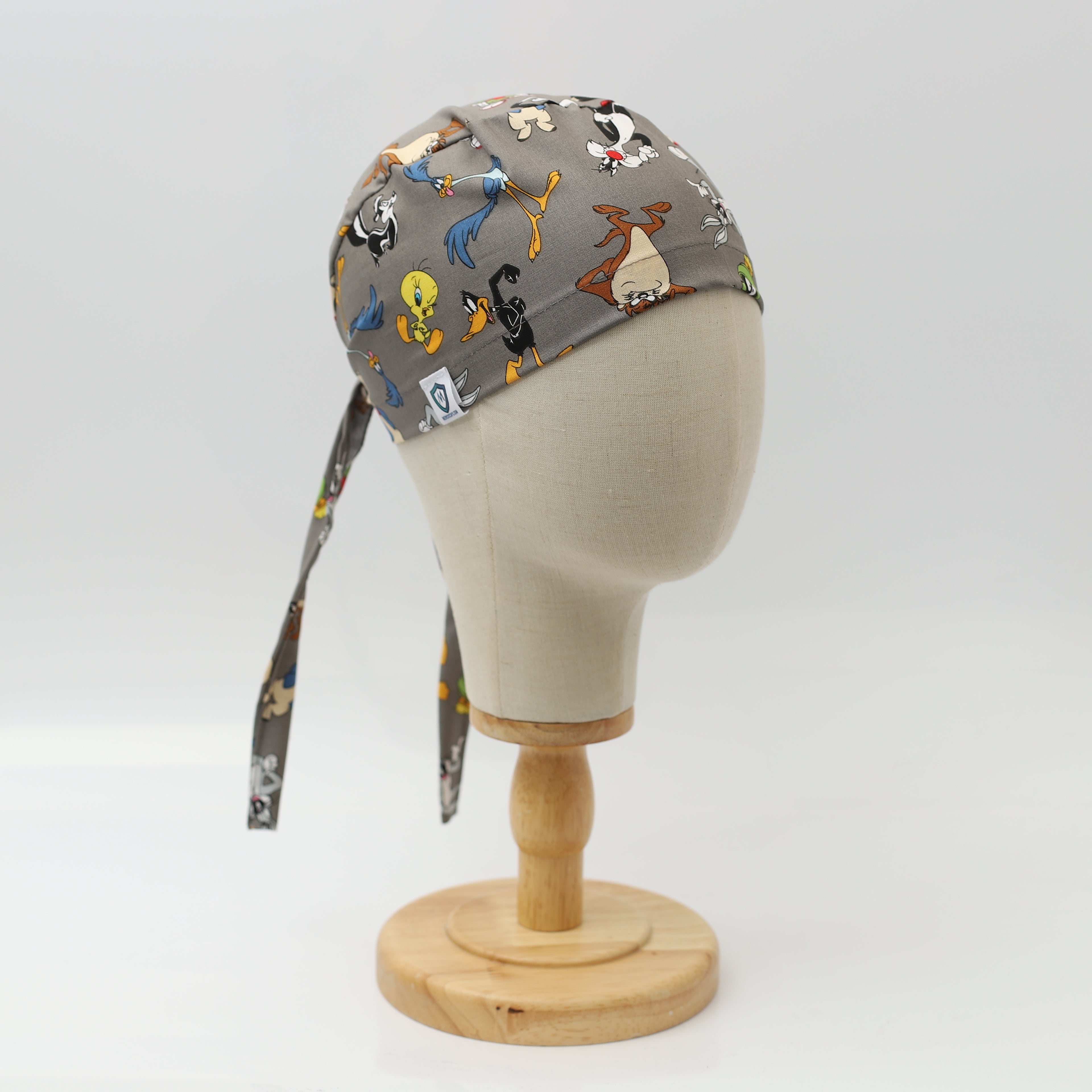 Grey Medicus Scrub Cap featuring a mashup of classic Looney Tunes characters, displayed on a mannequin head with tied straps.