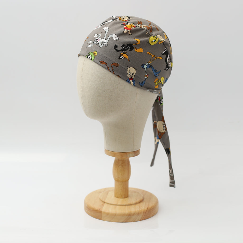Grey Medicus Scrub Cap featuring a mashup of Looney Tunes characters, displayed on a mannequin head with tie-back detail.