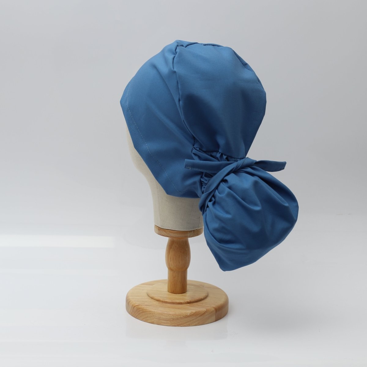 The Pony Scrub Cap in blue, displayed on a mannequin head, showcasing the tie-back design for secure fit and ponytail accommodation.