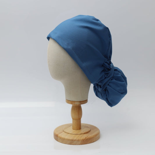 The Pony Scrub Cap in blue, displayed on a mannequin head, showcasing the left side view and its gathered back design for long hair.