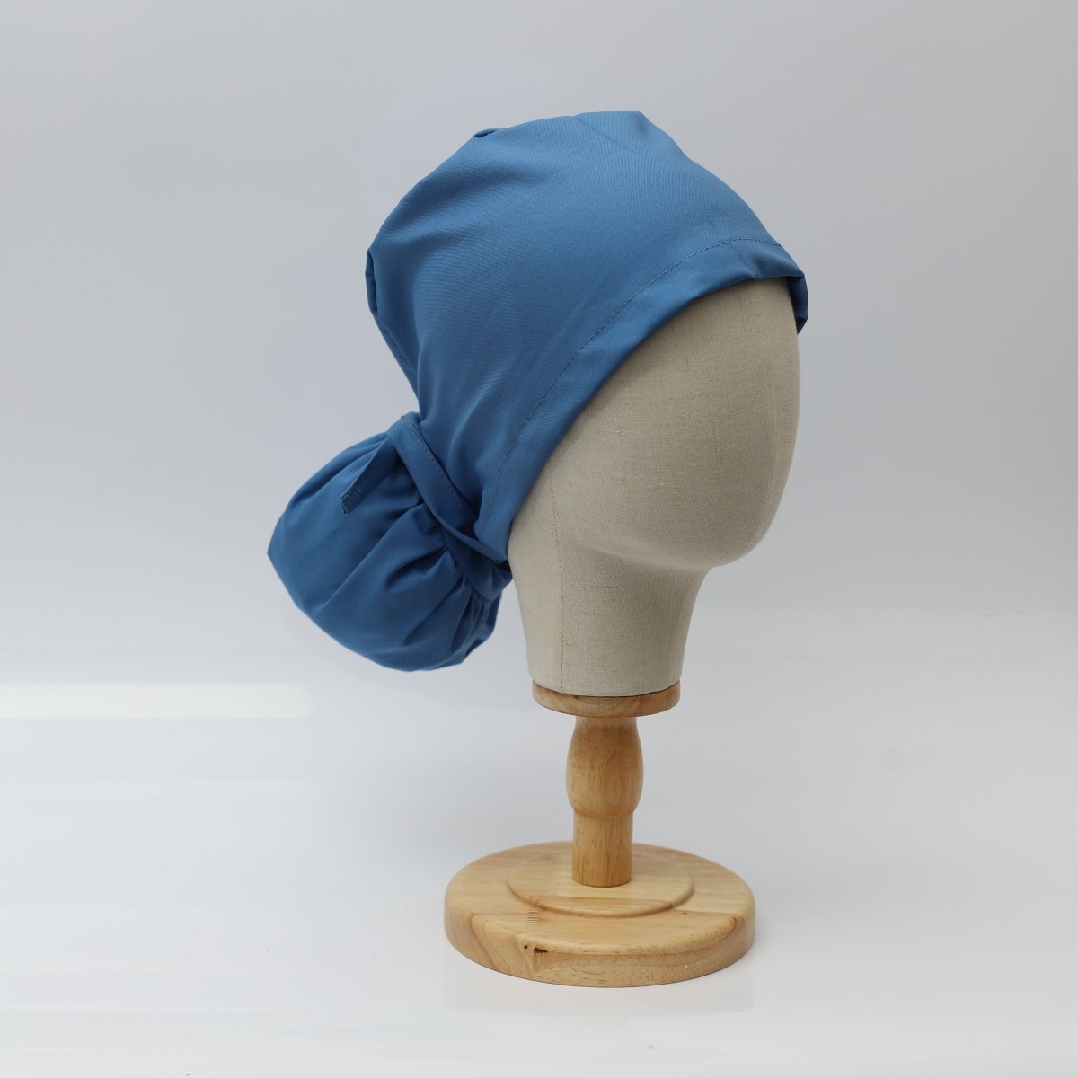 The Pony Scrub Cap in blue, displayed on a mannequin head, showcasing the right side view with a tied back design.