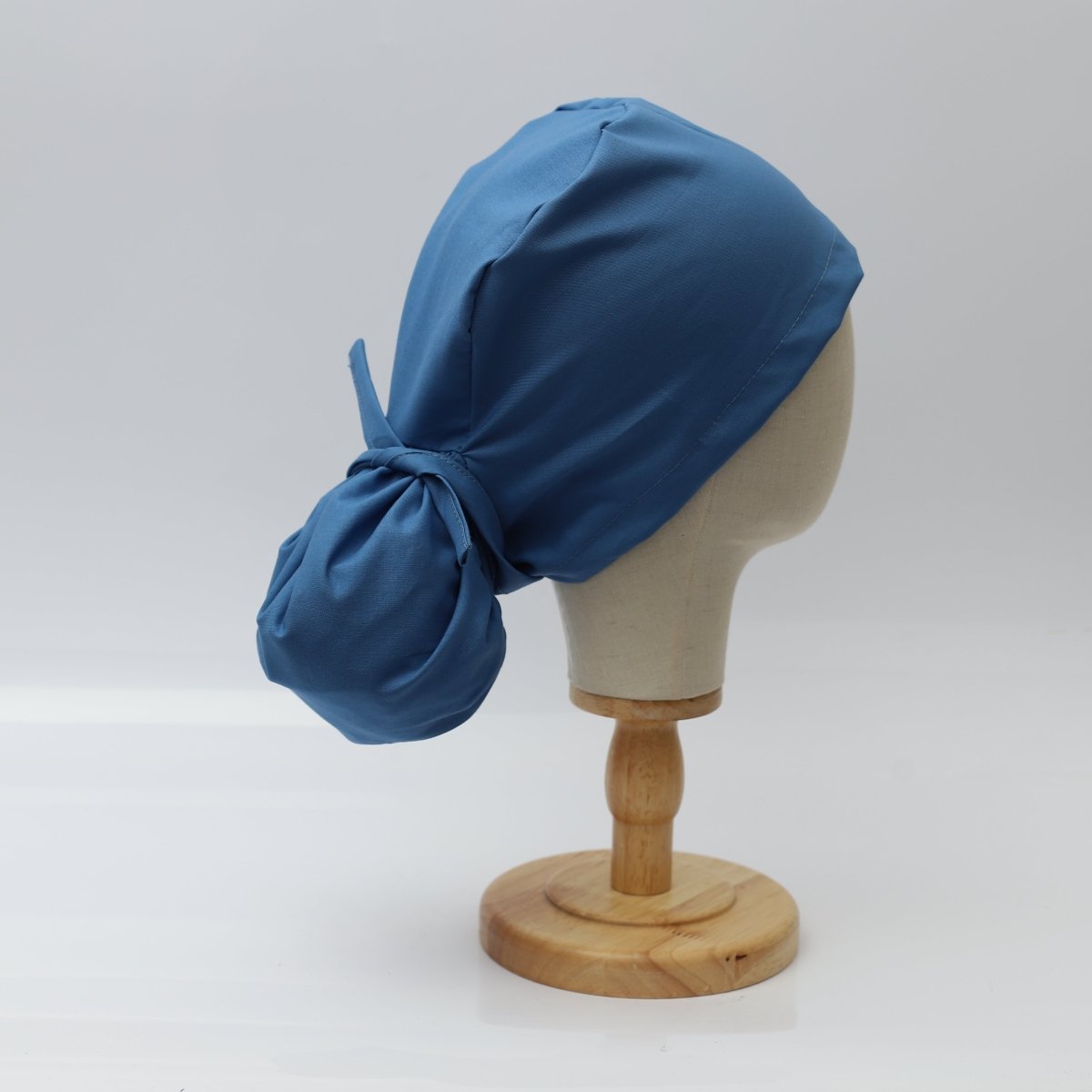 The Pony Scrub Cap in blue, displayed on a mannequin head, showing a right-side view with a tied-back pouch for long hair.