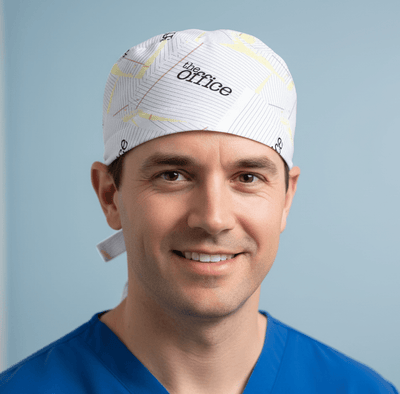 White paper airplane pattern scrub cap with yellow accents worn by smiling male healthcare worker