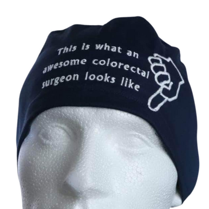A mannequin head wears a black Medicus Scrub Cap with custom embroidery reading, "This is what an awesome colorectal surgeon looks like," alongside a fist design.