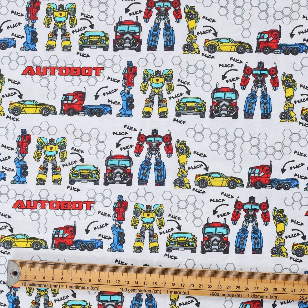 Close-up of Transformers Autobot builder vehicles pattern fabric with robots and trucks on white background and ruler for scale.