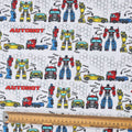 Close-up of Transformers Autobot builder vehicles pattern fabric with robots and trucks on white background and ruler for scale.