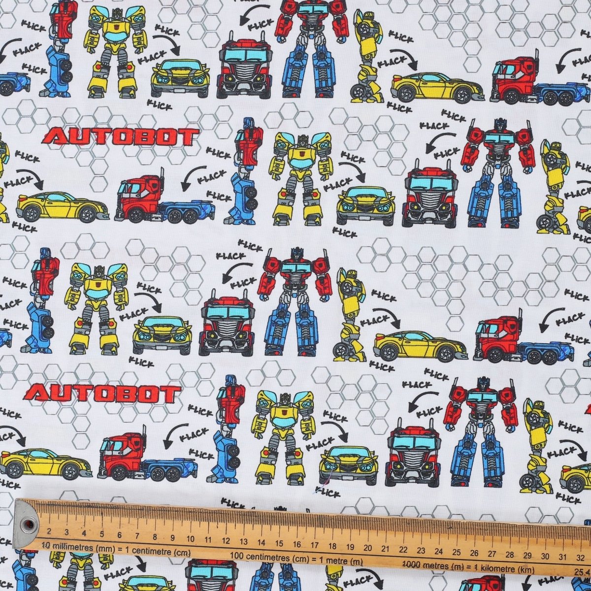 Close-up of Transformers Autobot builder vehicles pattern fabric with robots and trucks on white background and ruler for scale.