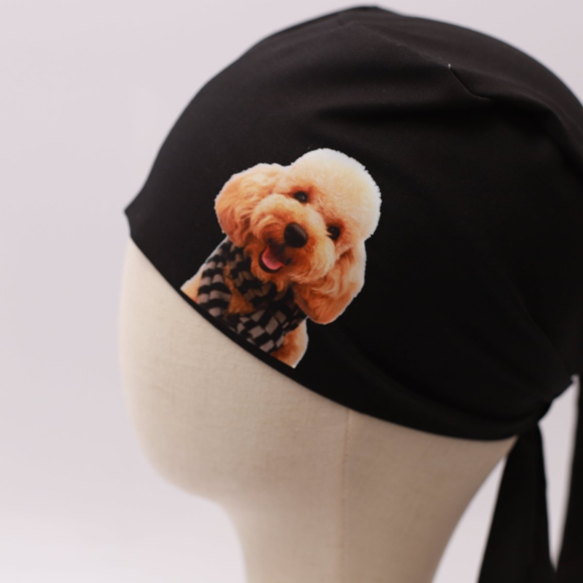 Black Medicus scrub cap with a vinyl sticker of a smiling poodle wearing a checkered scarf. Custom design by @scrub-caps-with-vinyl-stickers.