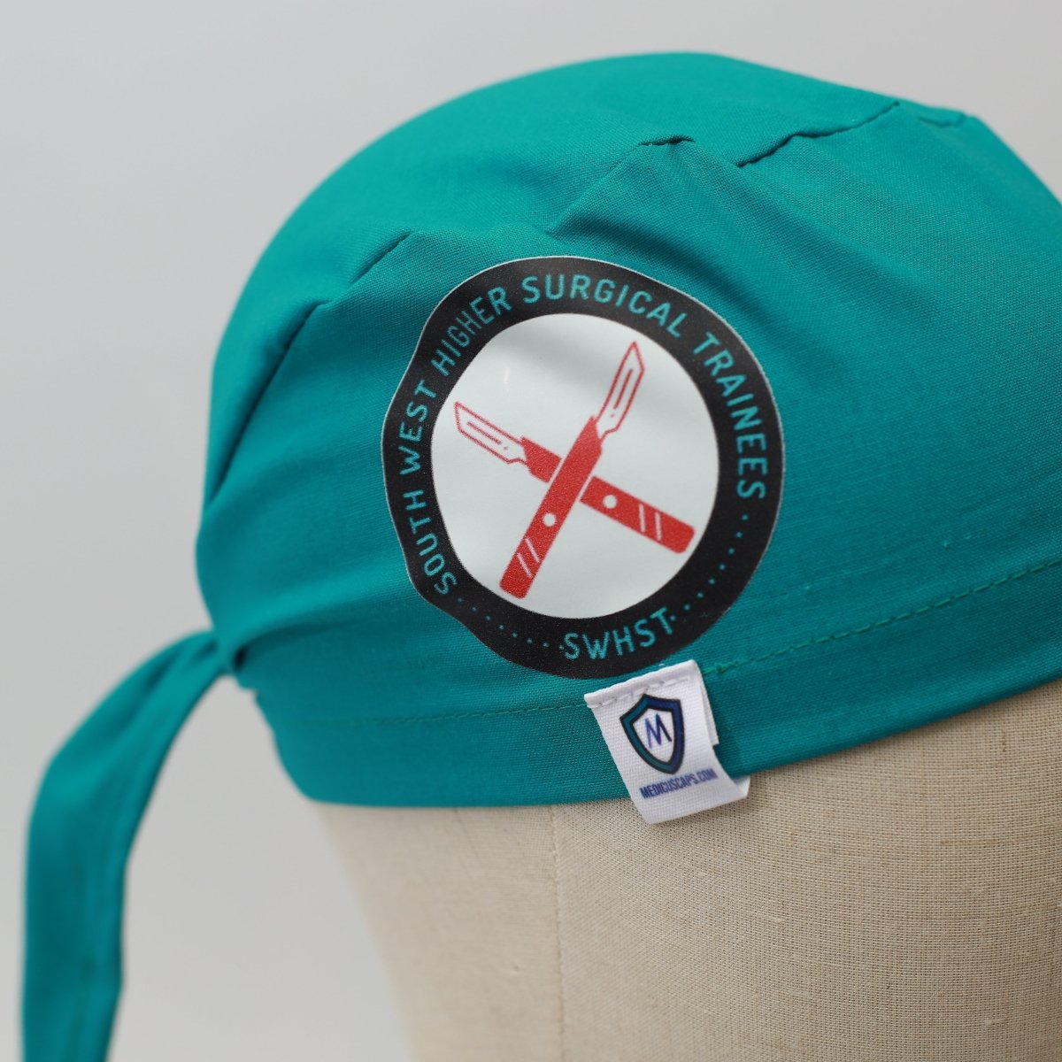 Teal Medicus Scrub Cap with a "South West Higher Surgical Trainees" vinyl sticker and Medicus tag, displayed on a mannequin. #scrub-caps-with-vinyl-stickers