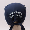 Navy blue Medicus scrub cap with custom vinyl text reading "John Smith Anaesthetist," tied at the back. From @scrub-caps-with-vinyl-stickers.