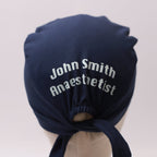 Navy blue Medicus scrub cap with custom vinyl text reading "John Smith Anaesthetist," tied at the back. From @scrub-caps-with-vinyl-stickers.