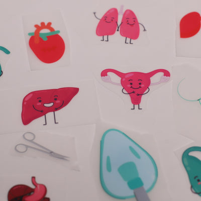 Premium DTF iron-on vinyl transfer examples showing cartoon medical organ designs ready to apply to scrub caps and garments