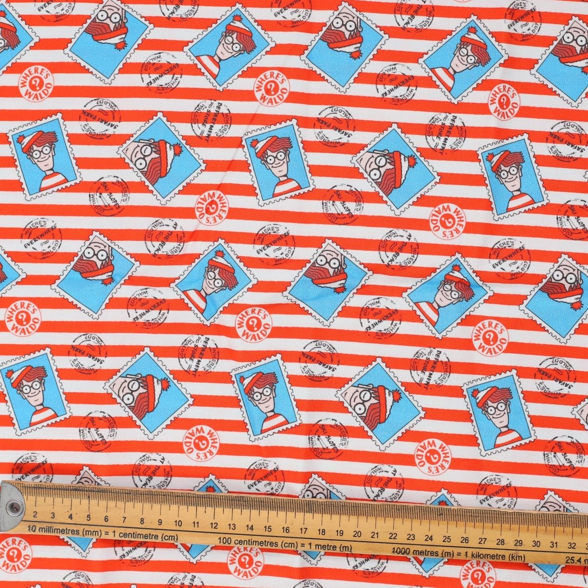 Close-up of Where's Waldo fabric with red-and-white stripes, turquoise framed Waldo illustrations and ruler for scale.