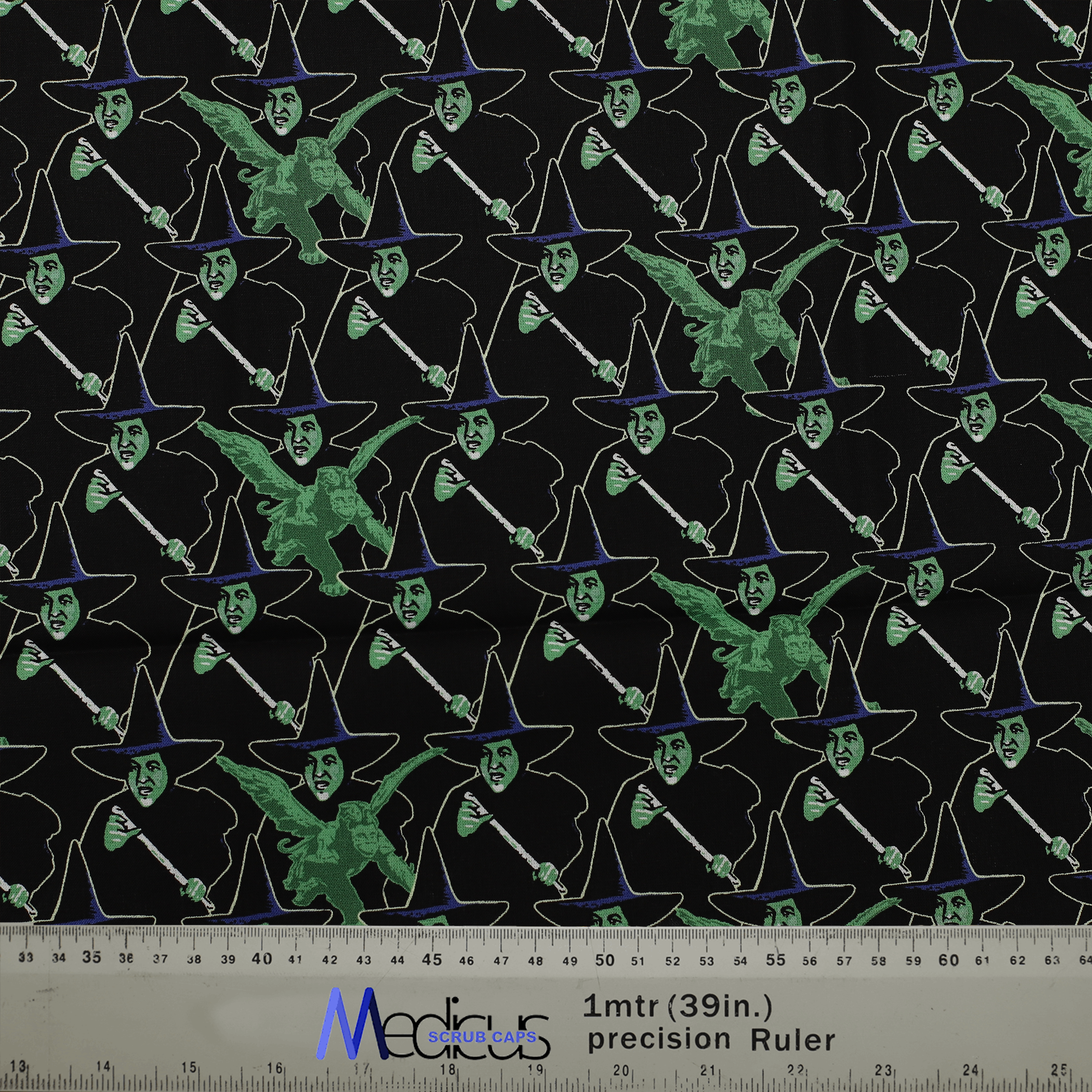 Fabric with a witch pattern for Medicus Scrub Caps, featuring green and black witches on a dark background with a ruler for scale.