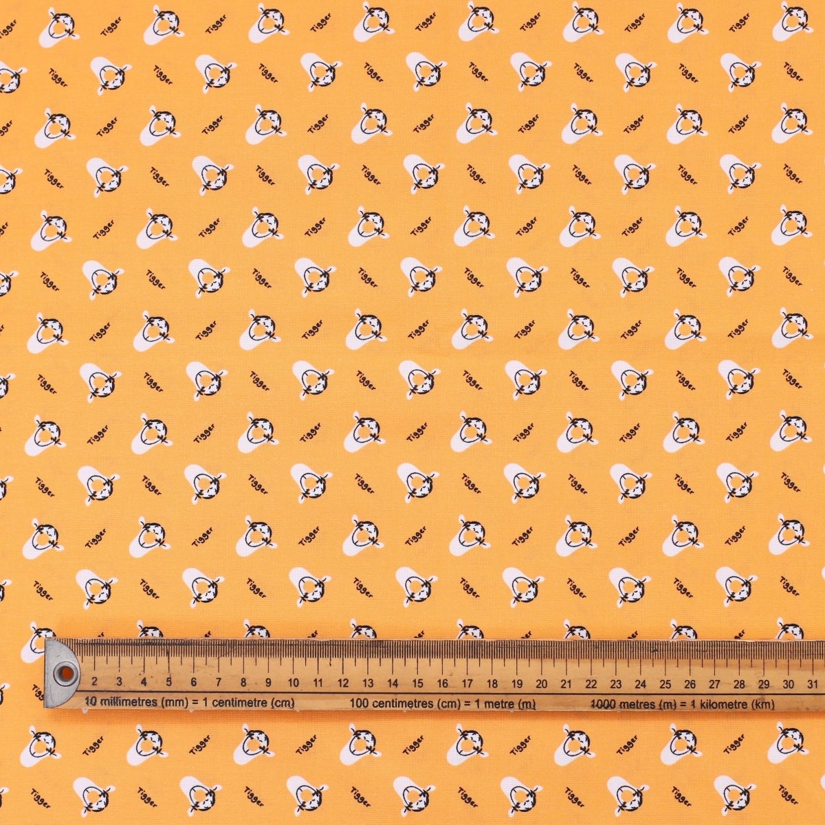 Patterned fabric with cartoon characters on a yellow background, ruler for scale.