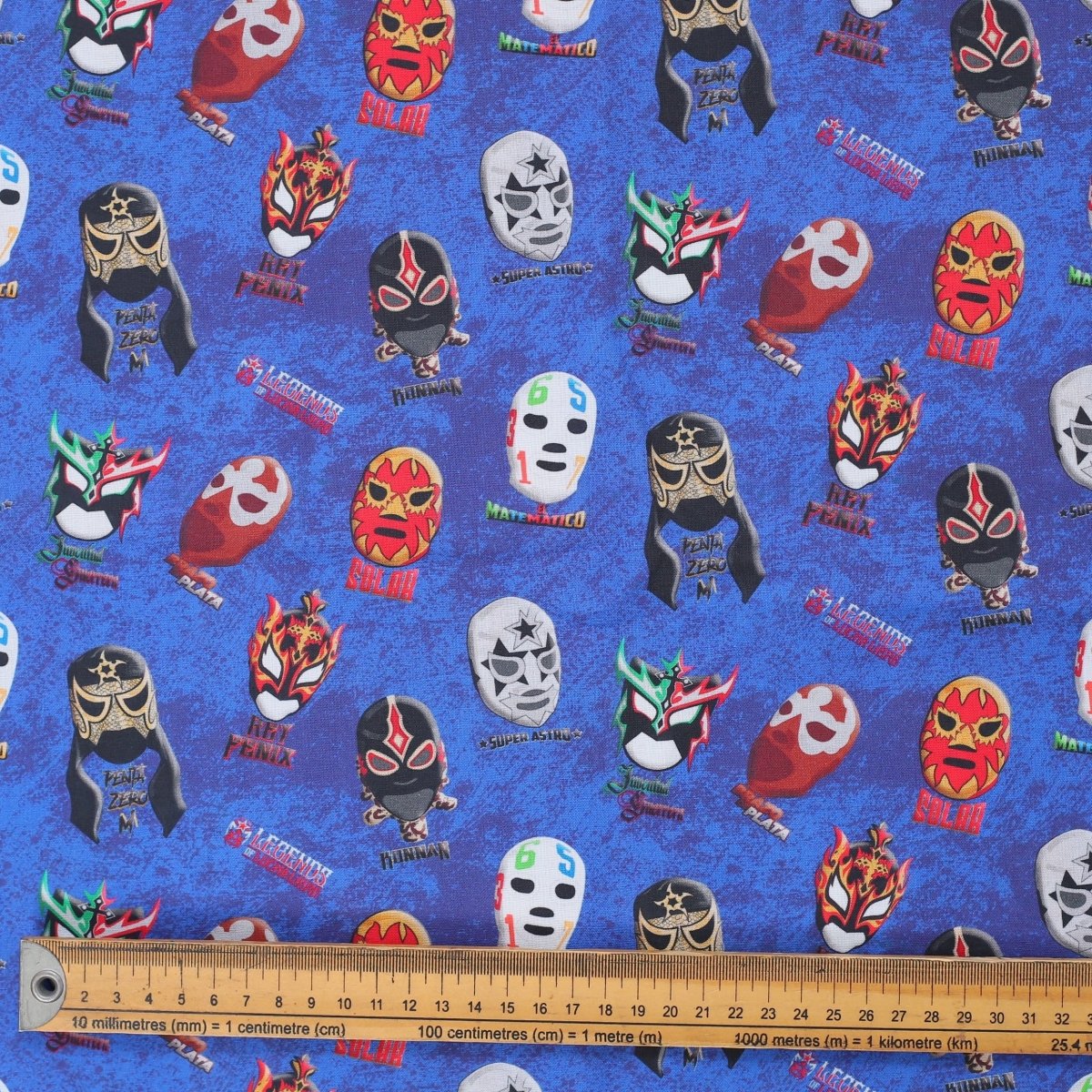 Close-up of blue scrub cap fabric featuring colorful wrestling masks with ruler for scale.