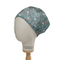 A mannequin head showcases a Medicus Scrub Caps sustainable Abstract Jungle Tooth Teeth scrub cap, set against a teal backdrop. The whimsical design features cute white teeth, roses, and dental tools with a copyright notice on the handcrafted dental headwear.