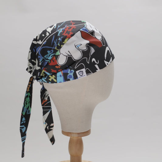 A mannequin head displays the All Over Custom Printed Fabric Scrub Cap by Medicus Scrub Caps. It features abstract patterns with gloved hands and shapes on multicolored fabric, tied at the back, against a plain white background.