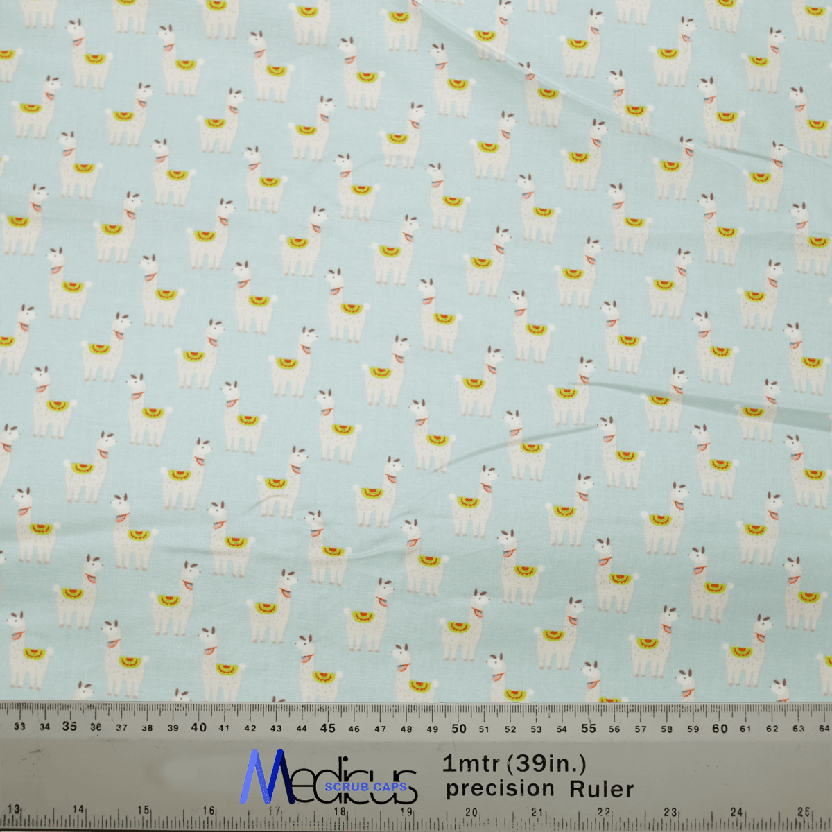 The whimsical Alpaca / Llama Party Blue Scrub Cap by Medicus Scrub Caps features cartoon llamas with saddles on a light blue fabric. Its perfect for medical attire, and a ruler at the bottom offers precise measurements in inches and centimeters, highlighting its detailed design.