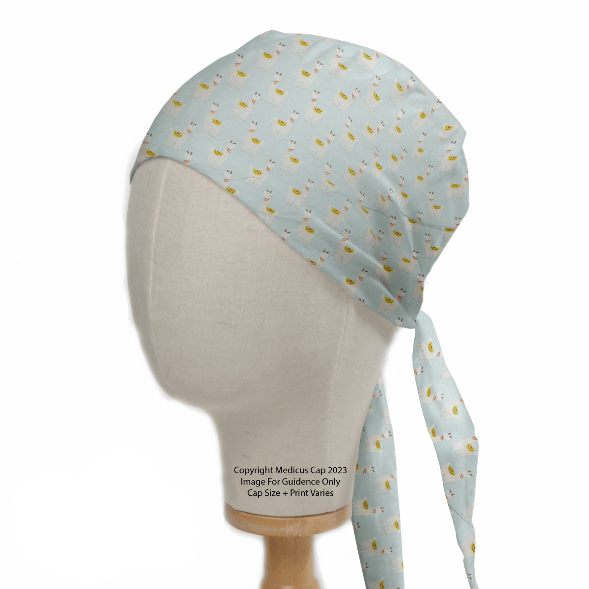 A mannequin head displays a light blue surgical cap with a fun pineapple pattern, made from eco-friendly materials. Resembling the Medicus Scrub Caps Alpaca/Llama Party Blue Scrub Cap, it has long ties and advisory text, with sizes and prints that may vary.
