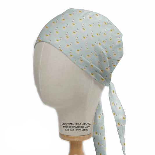 A mannequin head displays a light blue surgical cap with a fun pineapple pattern, made from eco-friendly materials. Resembling the Medicus Scrub Caps Alpaca/Llama Party Blue Scrub Cap, it has long ties and advisory text, with sizes and prints that may vary.