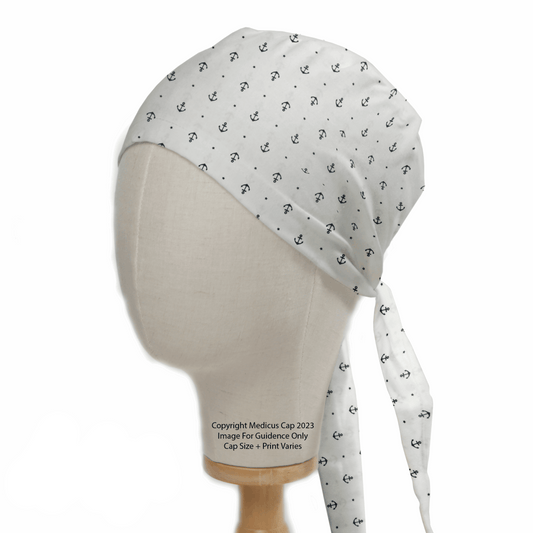 A mannequin head displays the Anchors On Ivory Scrub Cap from Medicus Scrub Caps, featuring small black anchor patterns. The cap ties neatly at the back, offering an inclusive sizing approach.