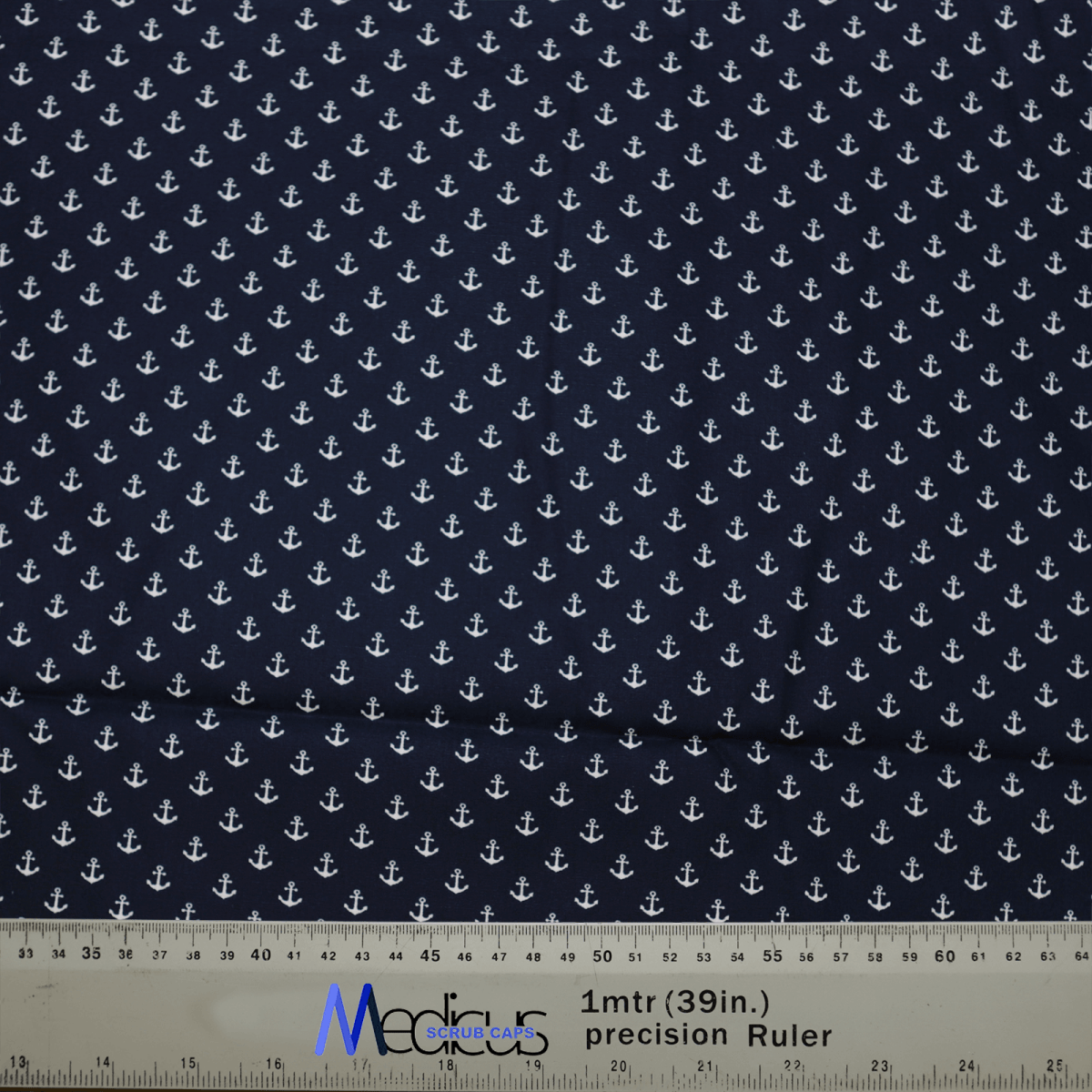 The Anchors On Navy Scrub Cap by Medicus Scrub Caps showcases a pattern of white anchors on dark blue fabric, designed to be eco-friendly and reusable. A ruler with centimeters and inches is visible below, partly revealing the Medicus label.