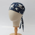 A mannequin head displays the Astronauts Spaceman Scrub Cap by Medicus Scrub Caps, featuring astronauts and celestial prints. Its mounted on a wooden stand against a plain white backdrop.