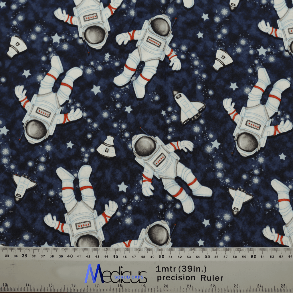 Medicus Scrub Caps Astronauts Spaceman Scrub Cap features a dark blue patterned fabric with cartoon astronauts in white spacesuits with red stripes, floating among stars and small space shuttles. A measuring ruler is included at the bottom for scale.
