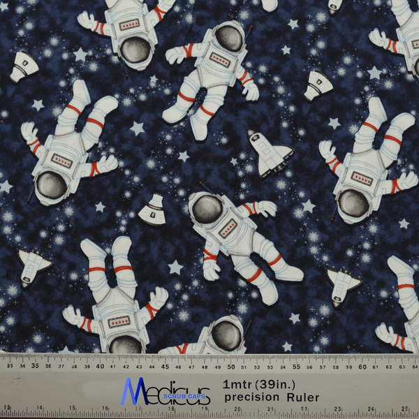 Medicus Scrub Caps Astronauts Spaceman Scrub Cap features a dark blue patterned fabric with cartoon astronauts in white spacesuits with red stripes, floating among stars and small space shuttles. A measuring ruler is included at the bottom for scale.