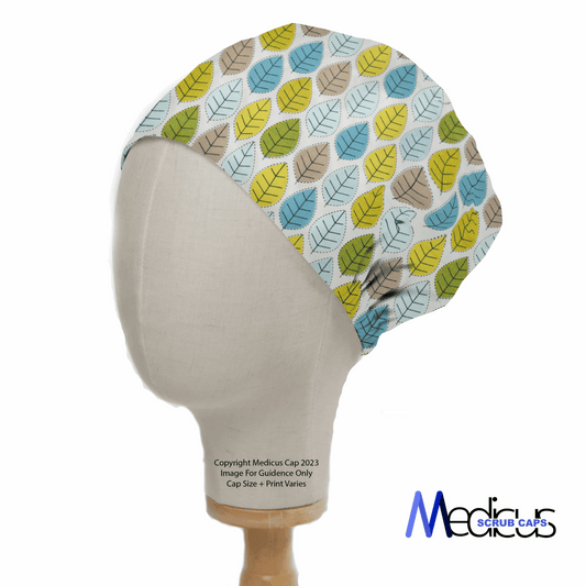 The mannequin displays the Autumn Leaves #1 Scrub Cap by Medicus Scrub Caps, featuring a vibrant leaf pattern in blues, greens, and yellows on a pale background. Text reads Copyright Medicus Cap 2023. Image for Guideline Only. Cap Size + Print Varies. Logo highlights the reusable design focus.