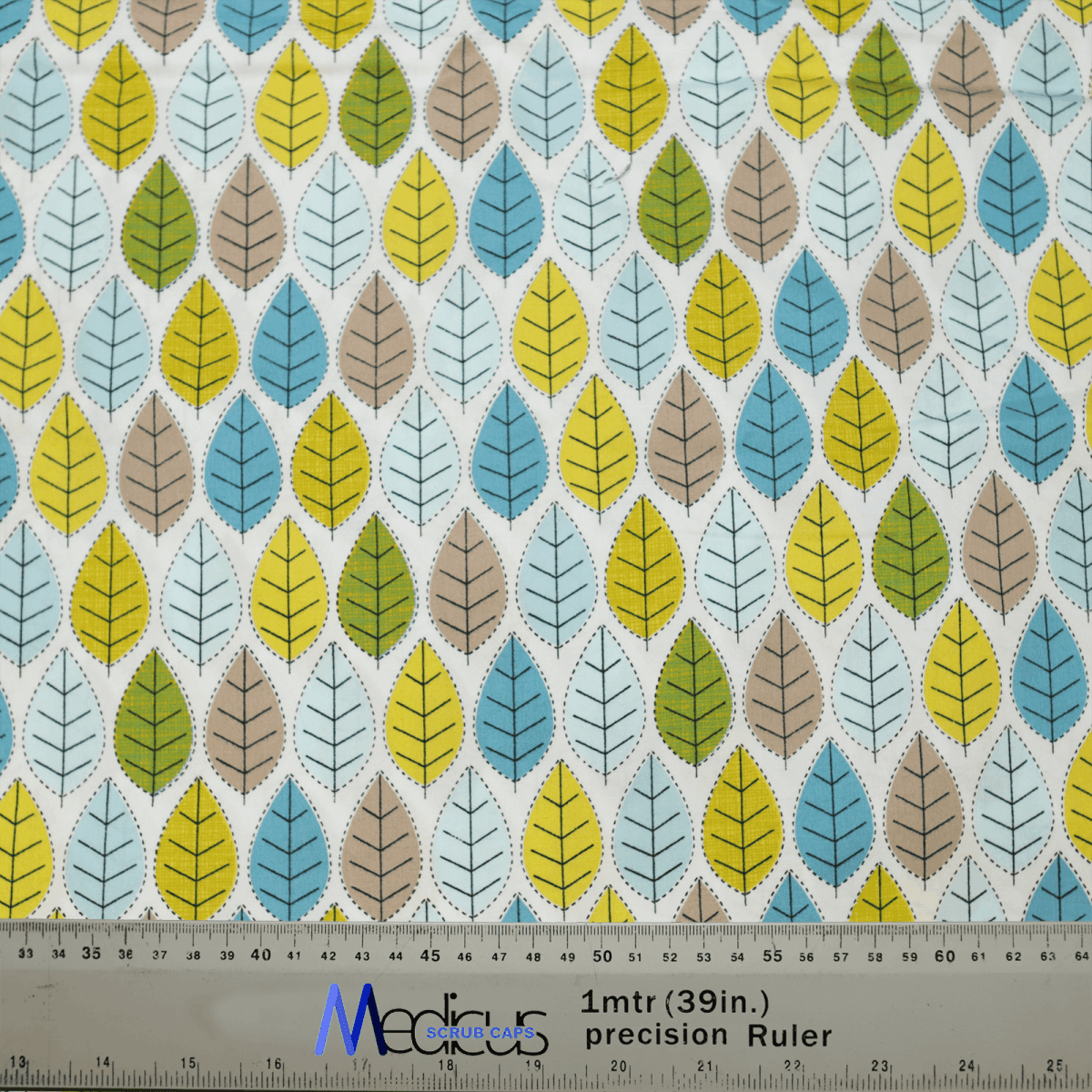 The Autumn Leaves #1 Scrub Cap by Medicus Scrub Caps features a backdrop of patterned fabric with green, blue, yellow, and brown stylized leaves. A ruler in centimeters and inches is included for crafting eco-friendly and stylish scrub caps.