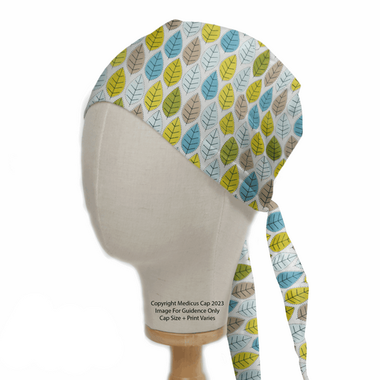 A mannequin displays the Autumn Leaves #1 Scrub Cap by Medicus Scrub Caps, featuring a vibrant pattern of blue, green, and yellow leaves on white. This sustainable cap has convenient tie straps at the back.