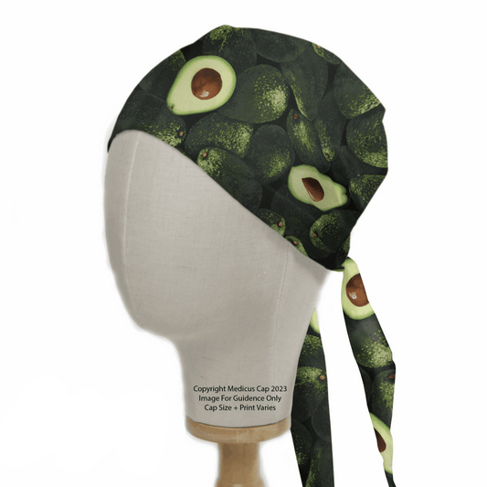 The Avocados Scrub Cap by Medicus Scrub Caps is displayed on a mannequin head, featuring whole and halved avocados against a dark background. This stylish cap combines healthcare professionalism with practical tie straps and highlights your dedication to sustainable fashion.