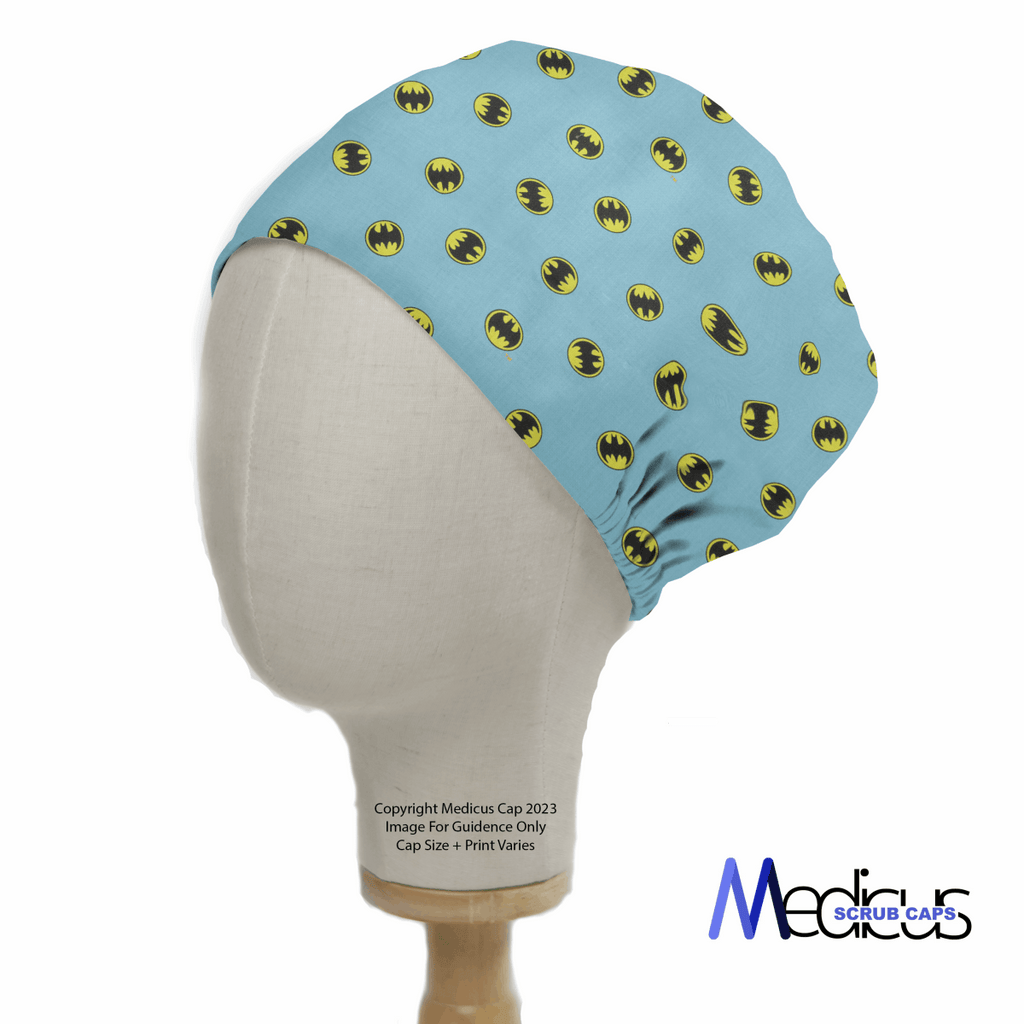 A mannequin head wears Medicus Scrub Caps Batman Signal On Blue featuring yellow and black bat symbols, celebrating healthcare heroism with its unique design and visible logo.