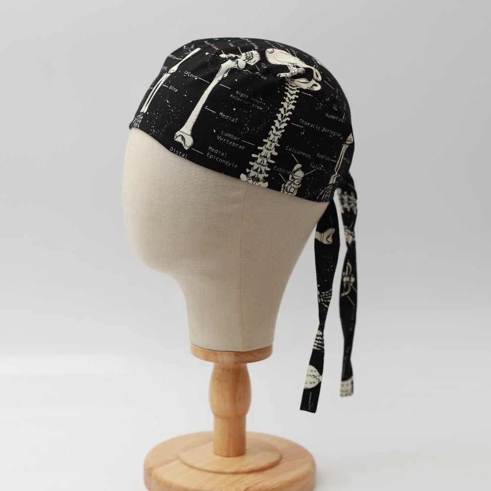 Mannequin head wearing Medicus Scrub Cap with skeleton-themed print, glow-in-the-dark, on a wooden stand against a white backdrop.