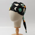Mannequin head wearing Medicus Scrub Cap with cartoon spaceships blue print, on a wooden stand against a white backdrop.