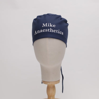 A mannequin head displays a navy cap from Medicus Scrub Caps, featuring high-quality fabric with Mike Anaesthetics embroidered in white, emphasizing its custom design against the plain white background.