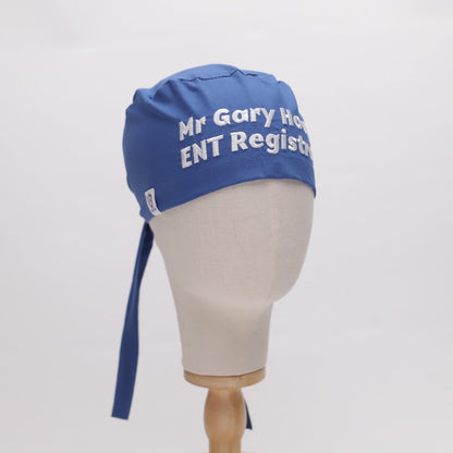 Mannequin head wearing a blue scrub cap with white embroidered text 'Mr Gary Hock ENT Registrar.'