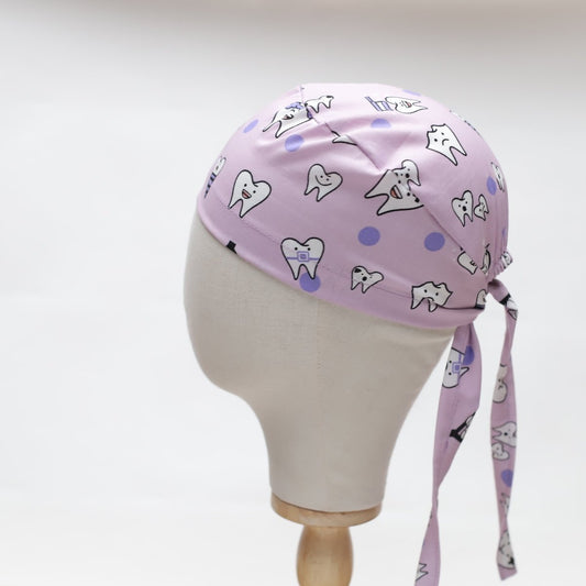 The Dentist Happy Teeth Purple Scrub Cap by Medicus Scrub Caps features cartoon teeth with radiant smiles and cheery purple polka dots, modeled on a mannequin head against a plain white background.