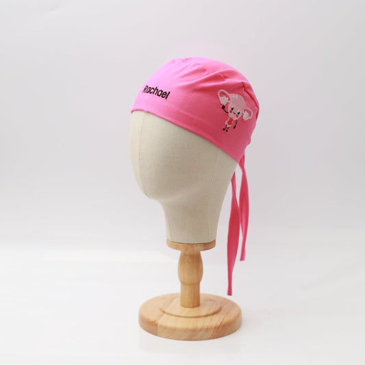 A mannequin head displays a pink Embroidery - Uterus - Scrub Cap by Medicus Scrub Caps, featuring a small cartoon rodent and the name Rachael embroidered on it. This reusable cap pops against the white background, providing style and personalization for medical professionals.