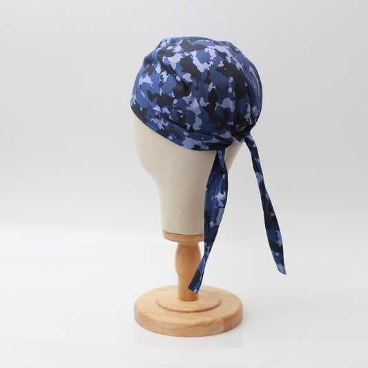 A Medicus Scrub Caps mannequin head displays the Military Camouflage Navy Scrub Cap, tied at the ends and elegantly placed on a wooden stand against a pristine white backdrop.