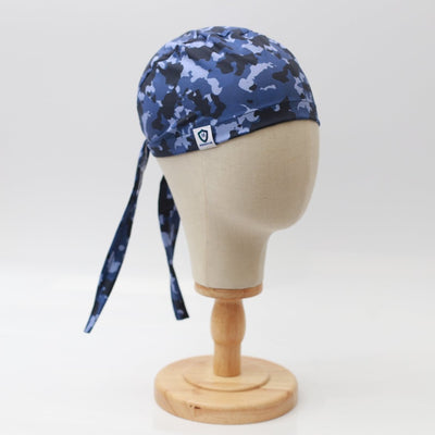 A mannequin head displays a Medicus Scrub Caps Military Camouflage Navy Scrub Cap, featuring long ties hanging elegantly down the back on a wooden stand against a plain white background.