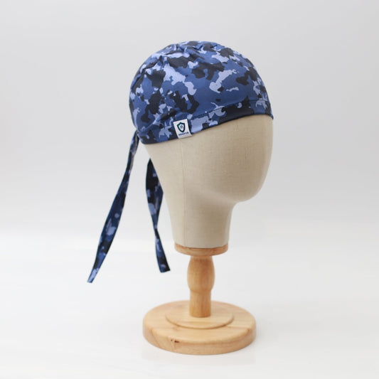 A mannequin head displays a Medicus Scrub Caps Military Camouflage Navy Scrub Cap, featuring long ties hanging elegantly down the back on a wooden stand against a plain white background.