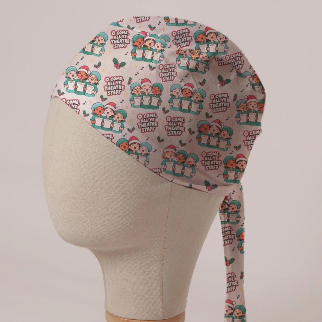 O Come All Ye Theatre Staff scrub cap: theatre staff in Santa hats singing carols from theatre lists with holly on pale grey