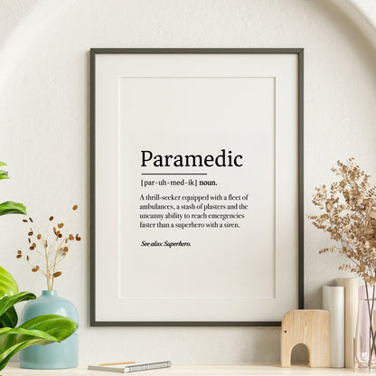 The Paramedic Definition poster by Medicus Scrub Caps humorously defines paramedics as superheroes with sirens. Displayed in a frame with plants and decor.