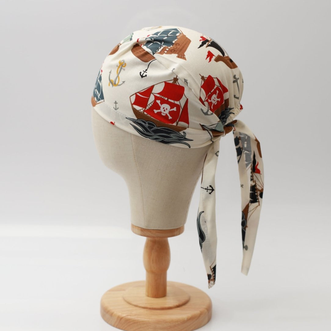 Mannequin head wearing Medicus Scrub Cap with pirate-themed print, on a wooden stand against a white backdrop.