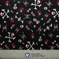 The black fabric features a pirate theme with white skulls and crossbones, some wearing red bandanas. Ideal for crafting a Pirate Skulls and Bones Scrub Cap by Medicus Scrub Caps. A bottom ruler provides measurements in inches and centimeters for precise hat customization.