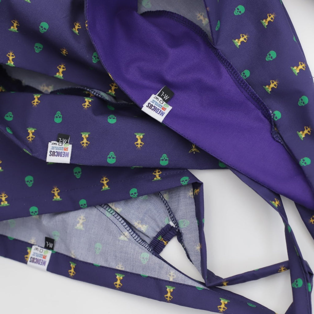 Close-up of reusable purple fabric with green skulls and yellow skeletons, ideal for scrub caps. The MEDICUS clothing label shows size M/L. The gathered material reveals different angles and textures.